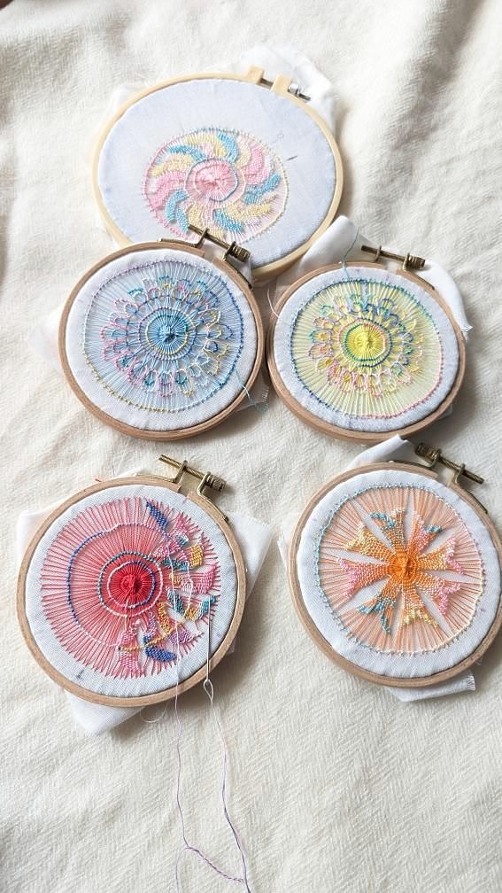 刺繍枠に張った布に、色糸で編んだ円形の模様。生成りのリネンの上に5つ並べている