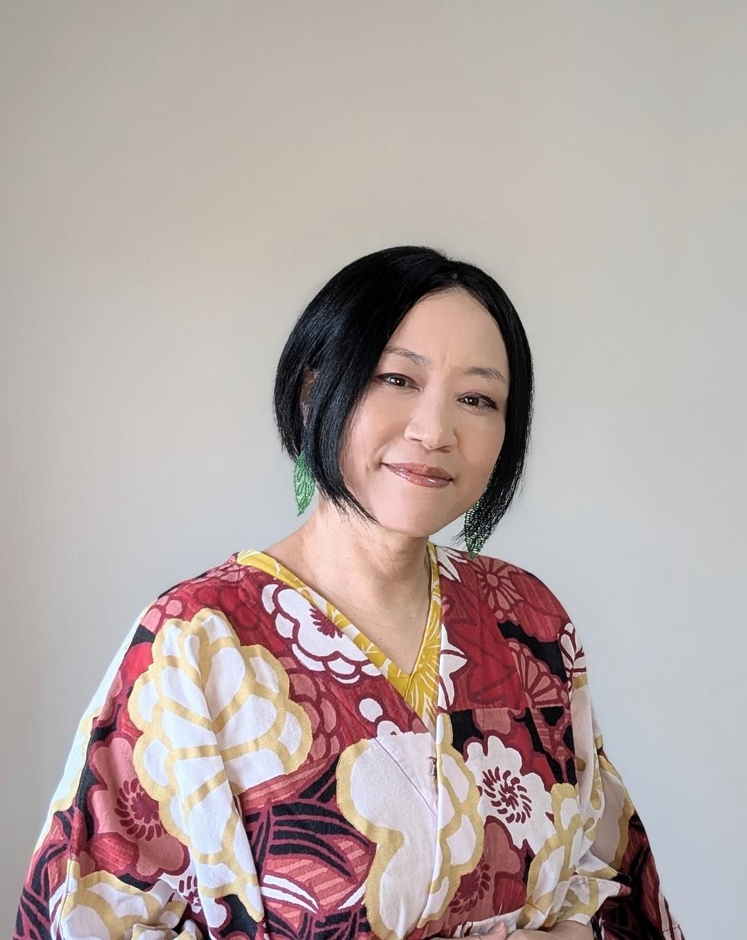手芸作家 片岡和美。赤い花柄の服で、葉の形の緑のピアスをつけている